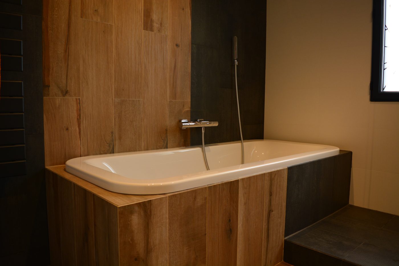 Baignoire encastrée dans un coffrage habillé de carrelage imitation bois, mitigeur thermostatique mural