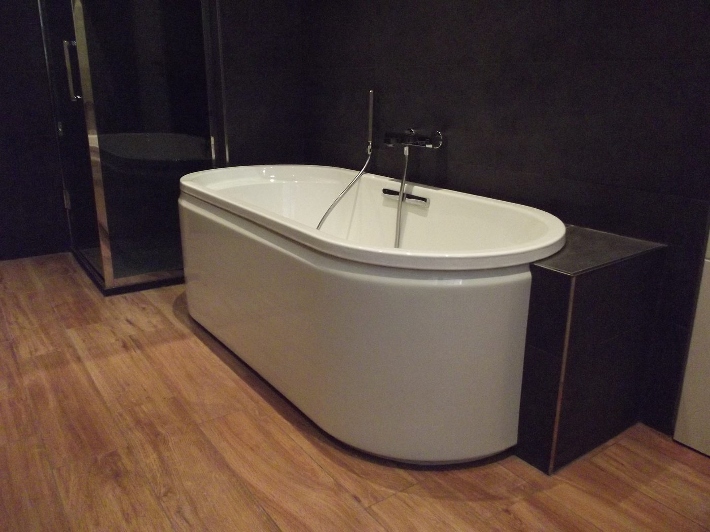 Baignoire semi-îlot adossée au mur, mitigeur et douchette muraux, joue carrelée et cabine de douche vitrée