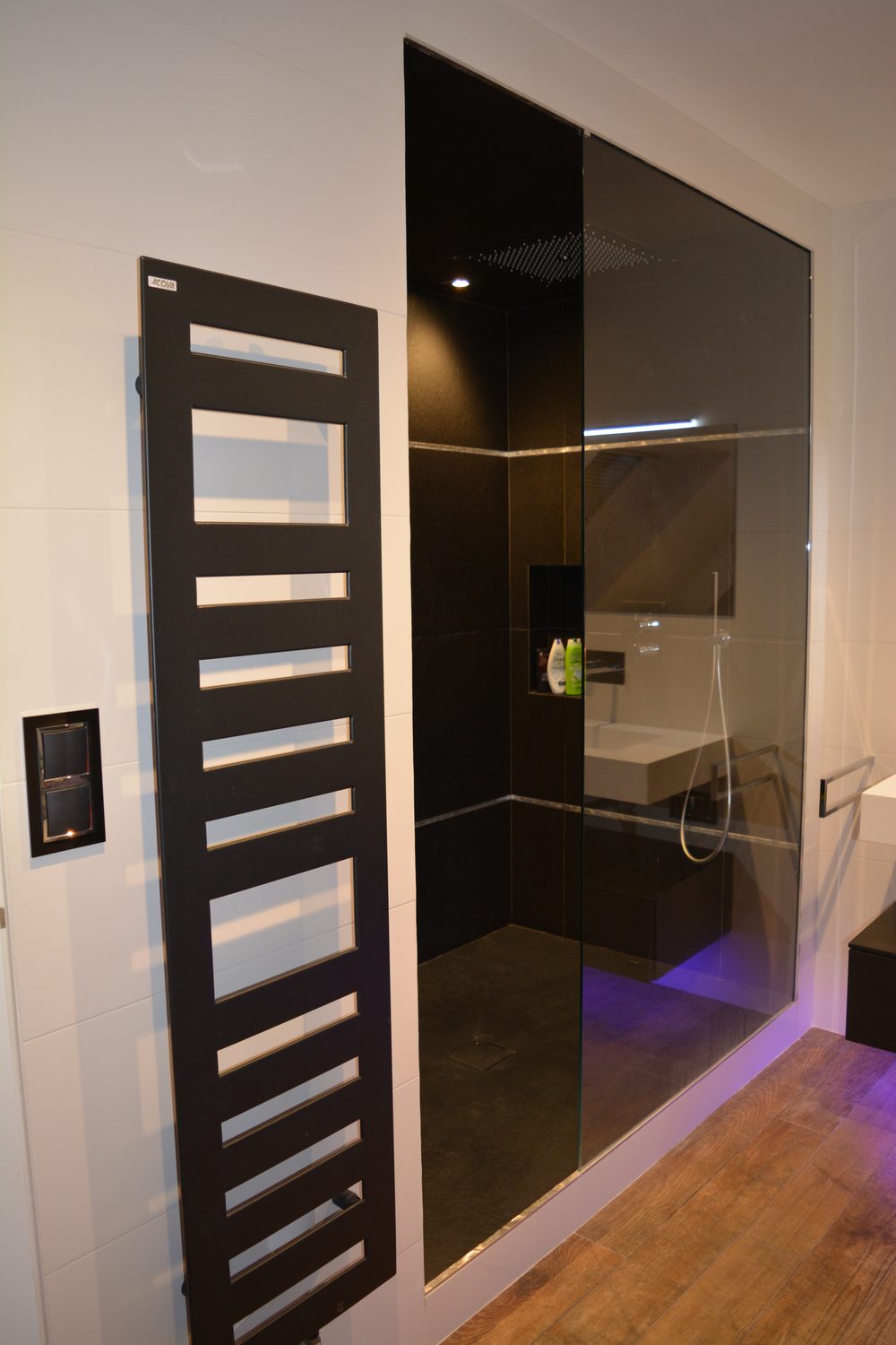 Douche à l'italienne en carrelage noir avec paroi en verre fumé, radiateur sèche-serviettes Acova noir
