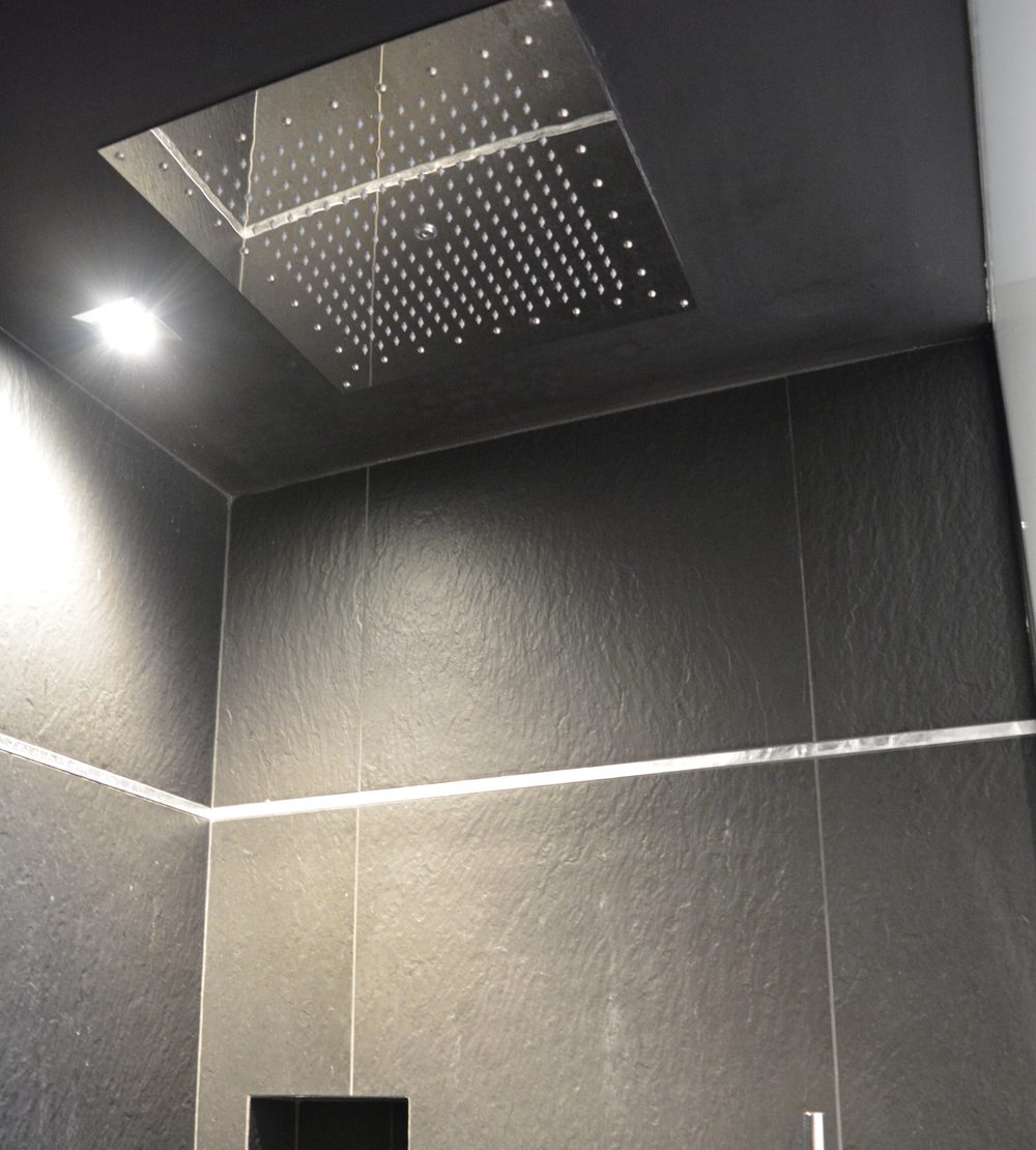 Pomme de douche carrée encastrée au plafond et carrelage noir effet ardoise avec listel métallique