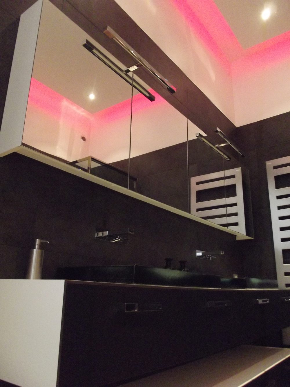 Faux plafond à gorge lumineuse LED rose au-dessus d'une armoire de toilette à miroirs