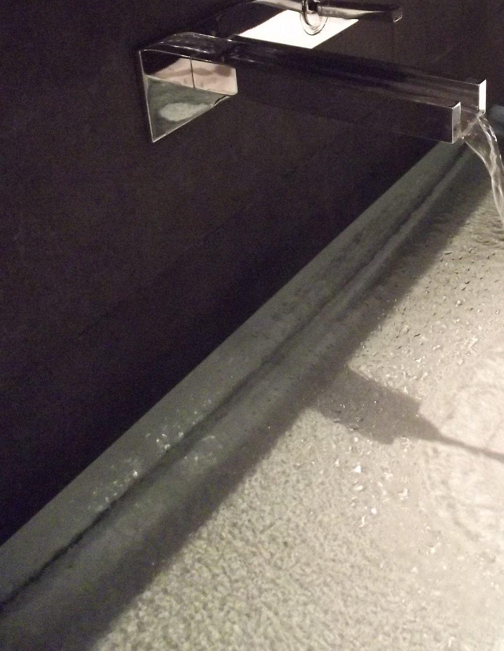 Robinet mural encastré à bec plat en cascade au-dessus d'une vasque en verre texturé