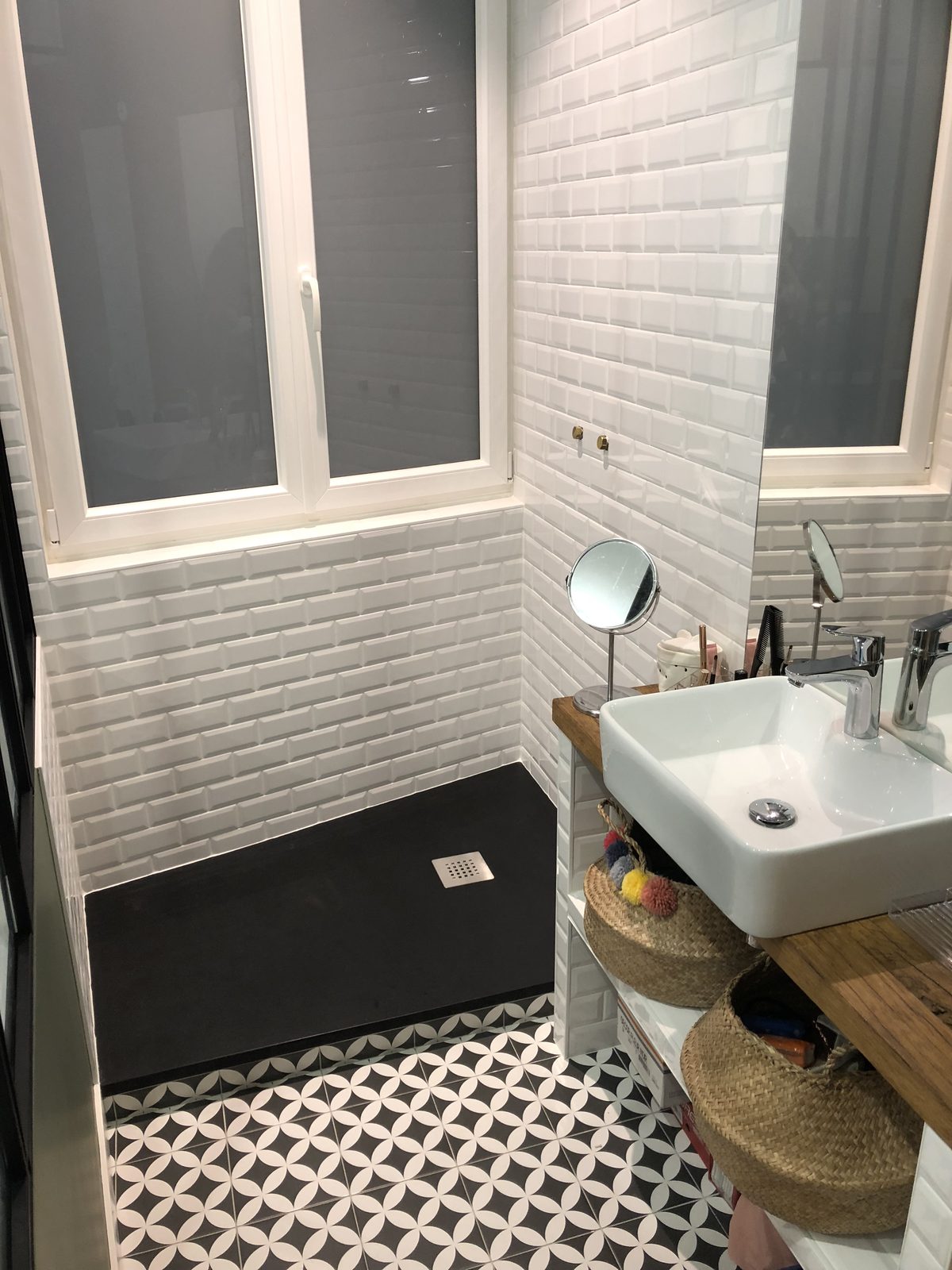 Receveur de douche noir découpé dans l'angle, support de vasque carrelé et carrelage au sol motif noir et blanc